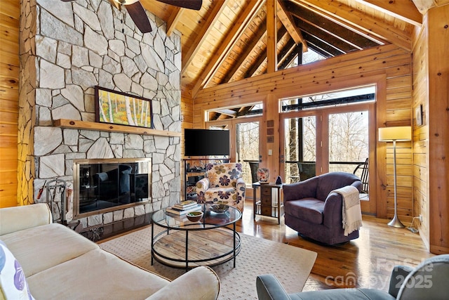 living area featuring wooden walls, wooden ceiling, wood finished floors, a stone fireplace, and beam ceiling