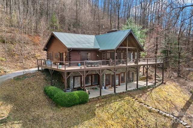 view of front facade featuring log siding, metal roof, a deck, a patio area, and a wooded view