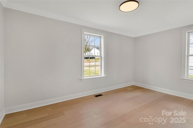 unfurnished room featuring light wood-style floors, a healthy amount of sunlight, visible vents, and baseboards