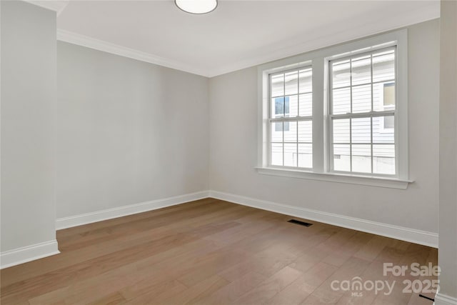 empty room featuring visible vents, crown molding, baseboards, and wood finished floors