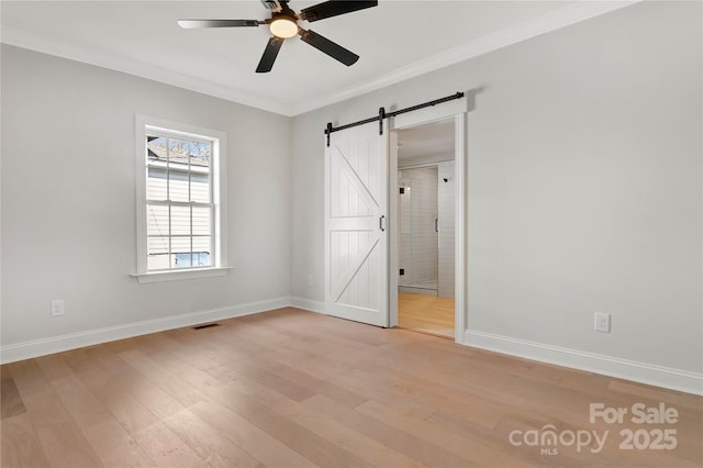 unfurnished bedroom with light wood-type flooring, a barn door, visible vents, and ornamental molding