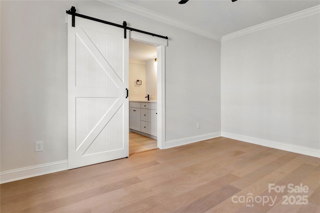 unfurnished bedroom with light wood-type flooring, crown molding, baseboards, and a barn door