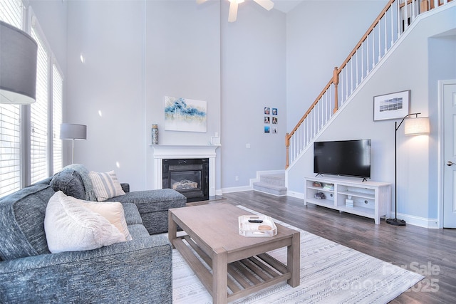 living room with stairs, wood finished floors, baseboards, and a towering ceiling