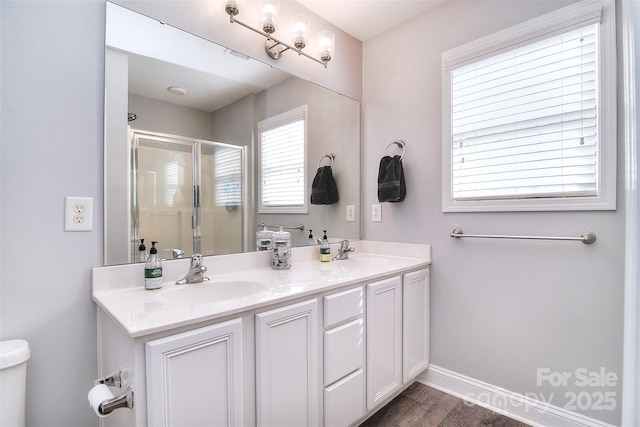 full bath with double vanity, a shower stall, wood finished floors, and a sink