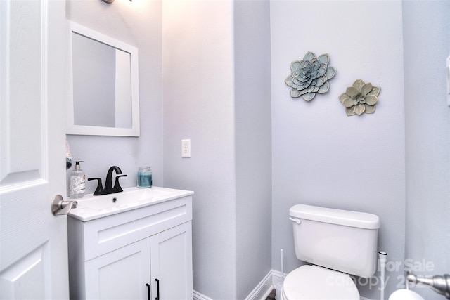 half bath featuring baseboards, toilet, and vanity