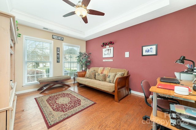 home office with light wood-style flooring, visible vents, a raised ceiling, and crown molding