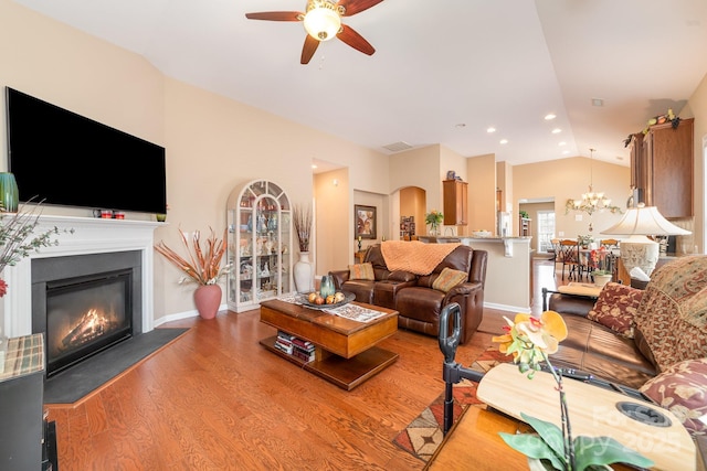 living area featuring lofted ceiling, ceiling fan with notable chandelier, visible vents, light wood finished floors, and a glass covered fireplace