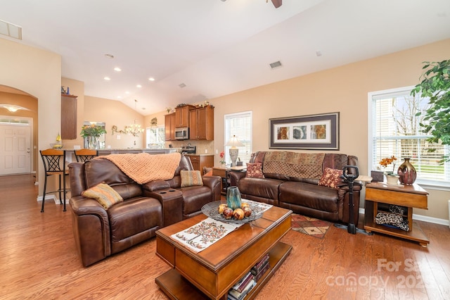 living room featuring light wood-style floors, visible vents, vaulted ceiling, and arched walkways