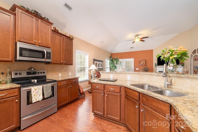 kitchen featuring light wood finished floors, stainless steel appliances, tasteful backsplash, vaulted ceiling, and a sink