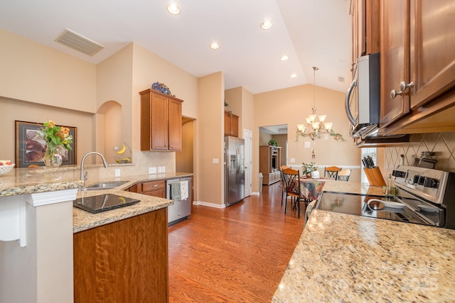 kitchen with stainless steel appliances, a peninsula, a sink, visible vents, and brown cabinetry