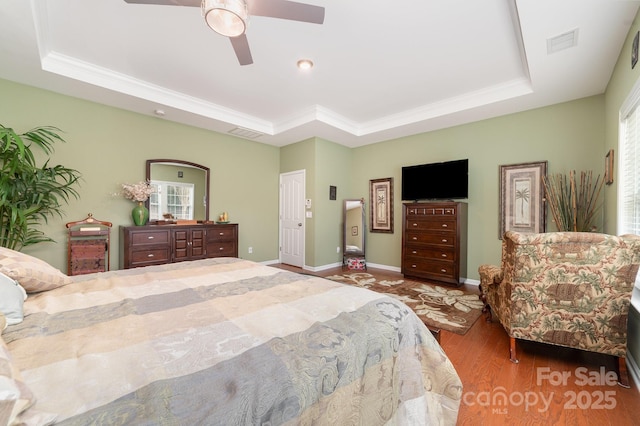 bedroom featuring a tray ceiling, visible vents, multiple windows, and wood finished floors