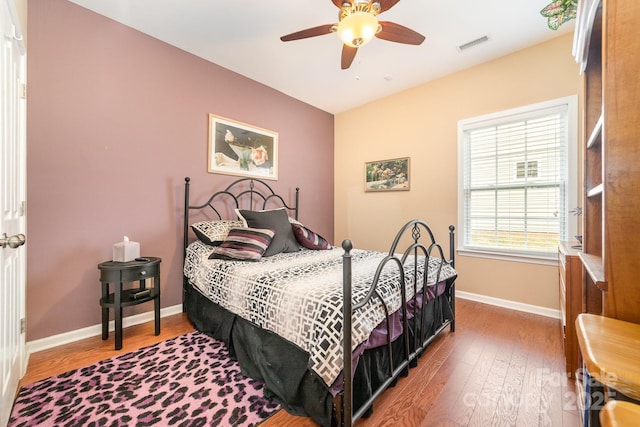 bedroom with ceiling fan, wood finished floors, visible vents, and baseboards