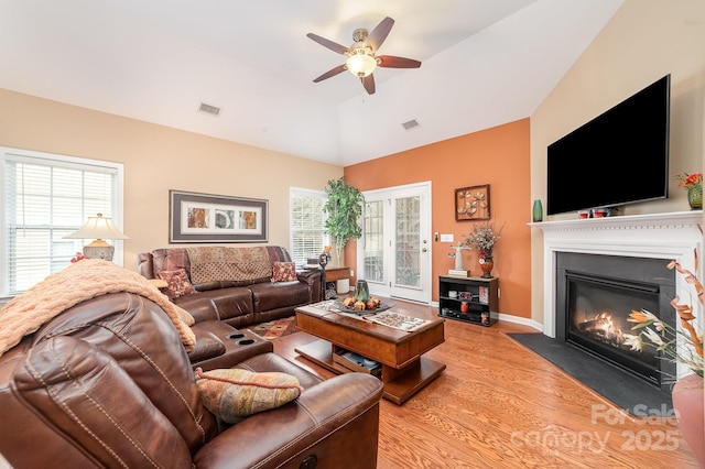 living area with visible vents, a ceiling fan, a fireplace with flush hearth, vaulted ceiling, and light wood-style floors