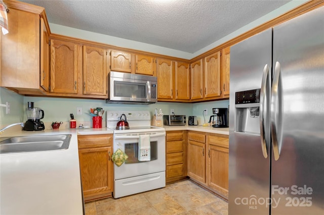 kitchen featuring light countertops, brown cabinetry, appliances with stainless steel finishes, and a sink