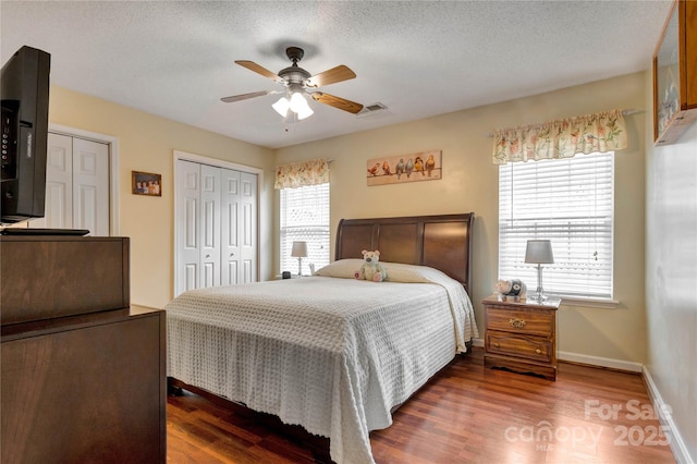 bedroom with baseboards, two closets, wood finished floors, and a textured ceiling