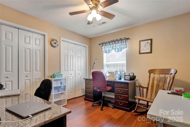 office featuring visible vents, a textured ceiling, ceiling fan, and wood finished floors