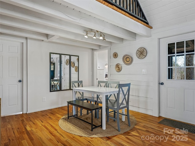 dining room featuring beam ceiling, light wood finished floors, and baseboards