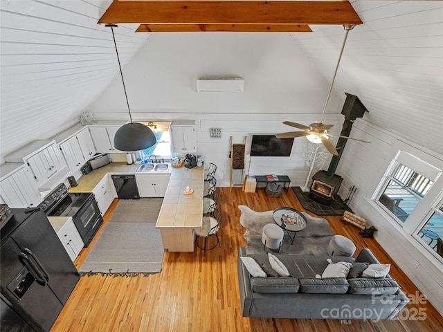 living room featuring beam ceiling, a wall unit AC, light wood-style floors, ceiling fan, and a wood stove
