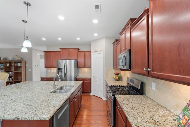 kitchen featuring stainless steel appliances, visible vents, a kitchen island with sink, a sink, and wood finished floors