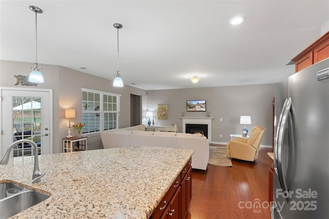 kitchen featuring a sink, a lit fireplace, freestanding refrigerator, dark wood finished floors, and decorative light fixtures