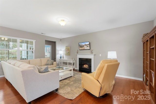 living area with a fireplace with flush hearth, visible vents, baseboards, and wood finished floors