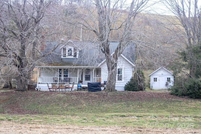 cape cod-style house featuring covered porch, a storage unit, and an outbuilding