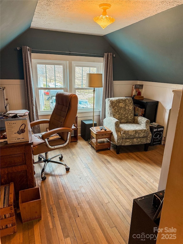 office featuring a wainscoted wall, a textured ceiling, vaulted ceiling, and hardwood / wood-style floors