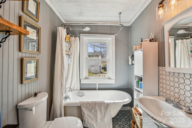 full bath with toilet, a sink, a textured ceiling, crown molding, and a freestanding bath