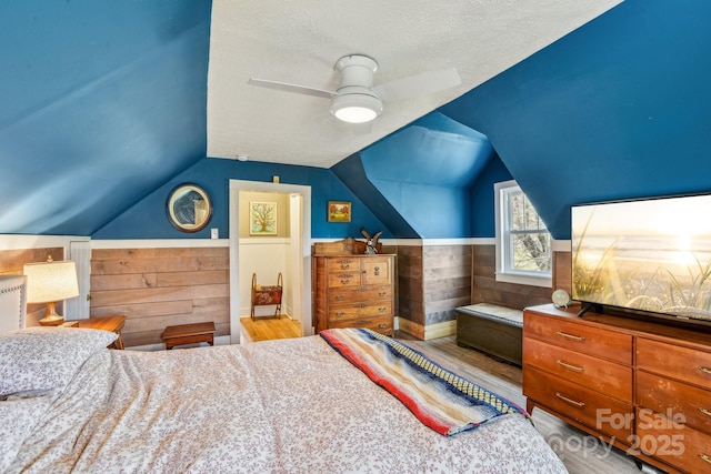 bedroom with lofted ceiling, wainscoting, wood finished floors, a textured ceiling, and a ceiling fan