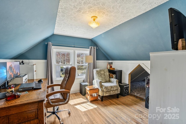 office area with a wainscoted wall, lofted ceiling, a textured ceiling, and hardwood / wood-style floors