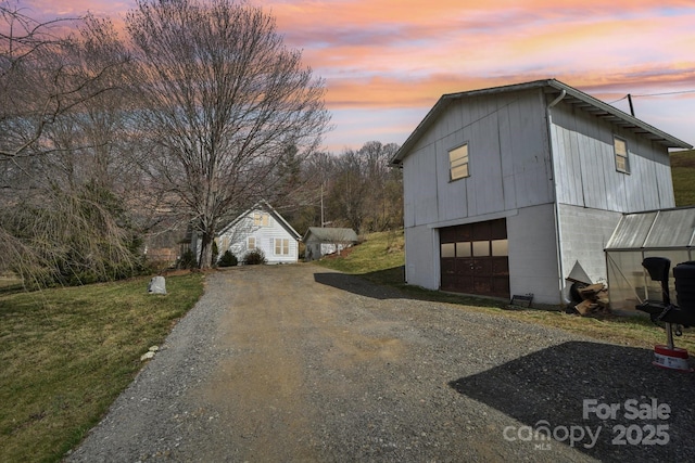 view of side of home featuring gravel driveway, an outbuilding, a lawn, and a garage