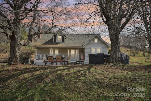 view of front facade featuring covered porch, a lawn, and roof with shingles