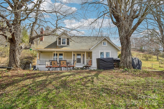 view of front of house with a shingled roof, a porch, a front yard, and a chimney