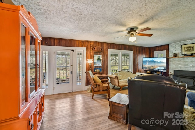 living room with plenty of natural light, light wood-style floors, a fireplace, and a ceiling fan