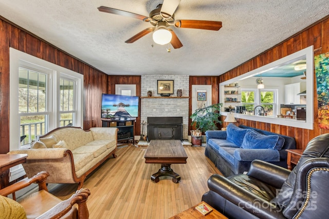 living room with wooden walls, a textured ceiling, light wood-style floors, and ceiling fan