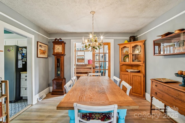 dining area with baseboards, a textured ceiling, light wood-style floors, and an inviting chandelier