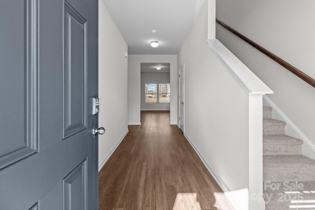 corridor featuring dark wood-type flooring, stairway, and baseboards