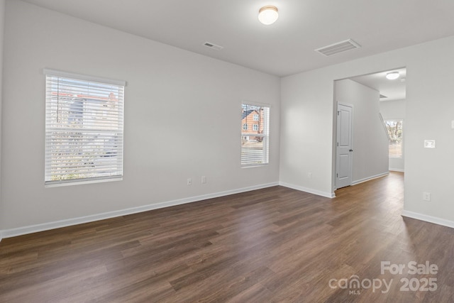 empty room with baseboards, visible vents, and dark wood-style flooring