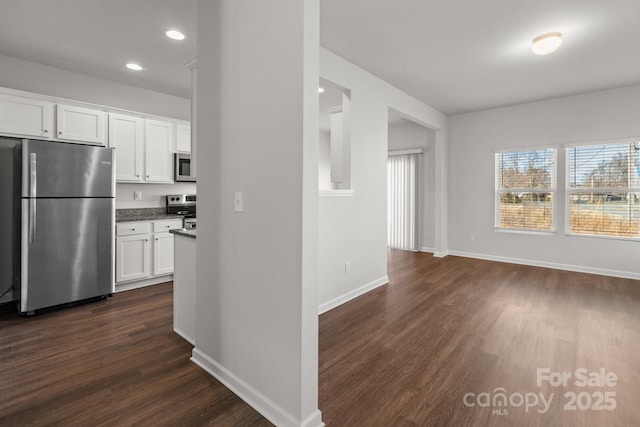 kitchen with appliances with stainless steel finishes, dark wood finished floors, white cabinetry, and baseboards