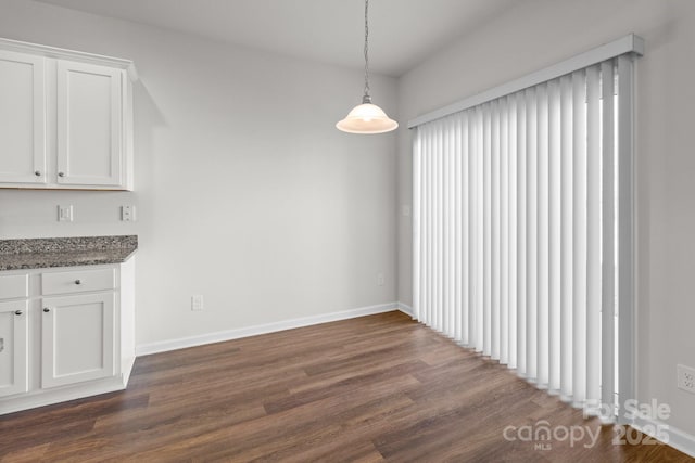 unfurnished dining area with dark wood-style floors and baseboards