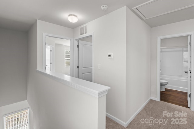 hall featuring carpet, an upstairs landing, visible vents, and attic access