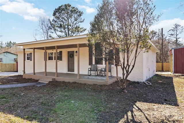 back of property featuring brick siding, a porch, and fence