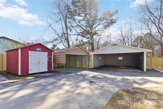 garage featuring driveway, a storage unit, fence, and a detached carport