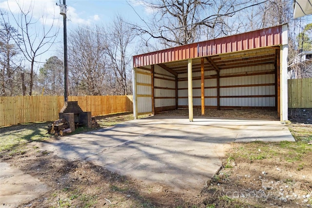 view of pole building with a carport, concrete driveway, and fence