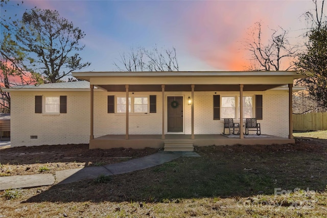 view of front facade with covered porch, brick siding, crawl space, and fence