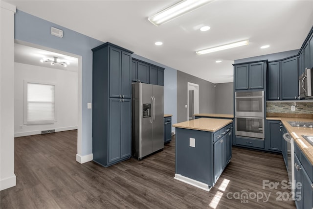 kitchen with a kitchen island, blue cabinetry, stainless steel appliances, dark wood-type flooring, and backsplash