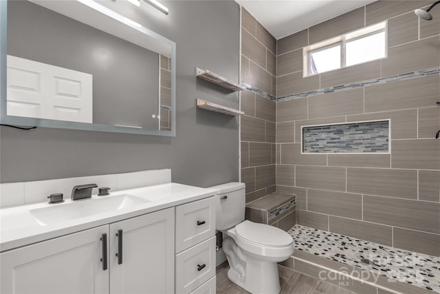 bathroom featuring toilet, vanity, and a tile shower