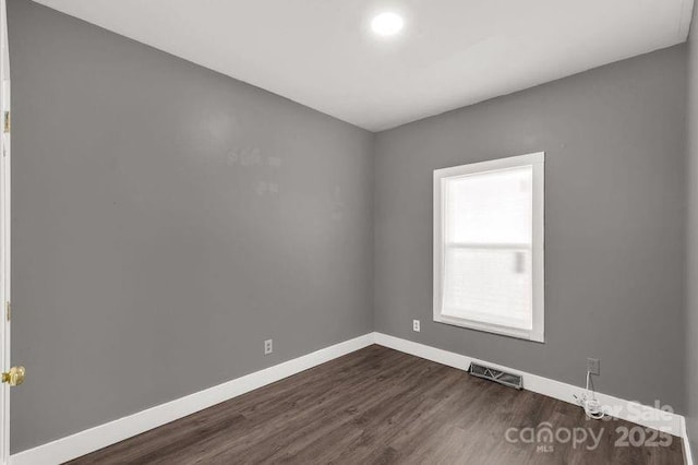 empty room featuring visible vents, dark wood-type flooring, and baseboards