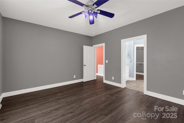 unfurnished bedroom with a walk in closet, dark wood-style floors, baseboards, and a ceiling fan