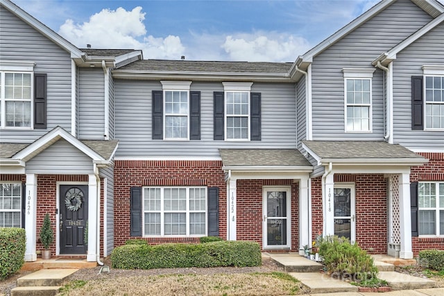 multi unit property featuring a shingled roof and brick siding